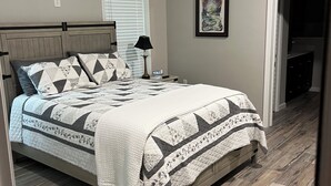 A bedroom with a bed, a ceiling fan, a nightstand, a lamp, a framed picture, and a door leading to another room.