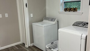 A laundry room with a washer and dryer, a window with a view of greenery, and a wooden floor.
