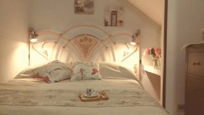 A neatly made bed with floral bedding, a bedside table with a cup and saucer, and a wall-mounted lamp. - Cicci's house (Cefalù)