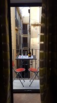 Un balcón con una mesa, dos sillas rojas y una botella de vino.