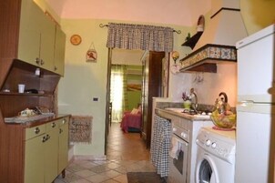 Cocina compacta con lavadora, un lavamanos y una pequeña encimera. Hay una puerta que da a otra habitación.