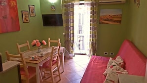 A dining area with a table and chairs, a TV mounted on the wall, and a sofa with floral cushions. - Cicci's house (Cefalù)