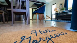 A doormat with "Hello Gorgeous" written on it, a blue chair, a staircase, and a piano in a living room. - Gorgeous Ocean View Rooftop Patio, Private gated 2 bedroom home, Walk to beach (Coco)