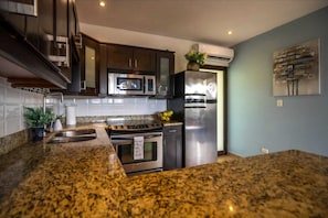 A modern kitchen with granite countertops, stainless steel appliances, and dark cabinetry. - Gorgeous Ocean View Rooftop Patio, Private gated 2 bedroom home, Walk to beach (Coco)