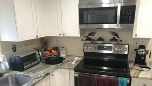 A kitchen with white cabinets, a microwave, a toaster, a stove, and a coffee maker. - Tampa Lakehouse 6-bedroom houses on a acre (Tampa)