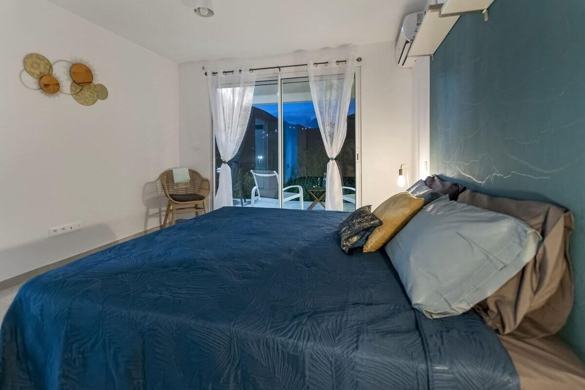 Un dormitorio con una cama grande, una silla y vistas al exterior a través de un ventanal corredero.