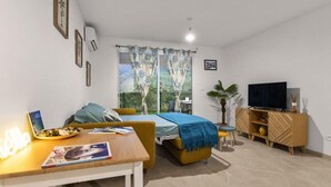 Una sala de estar moderna con un sofá, una mesa de comedor, un televisor y un balcón con cortinas.
