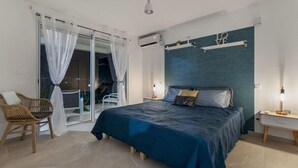 Un dormitorio con una cama, una silla, una mesita de noche y vistas a través de un ventanal.