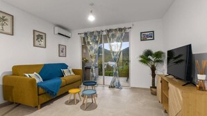 Una sala de estar con un sofá, mesitas, un televisor y una planta.