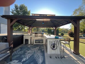 An outdoor kitchen with a grill, bar area, and seating under a pergola. - Plenty of room for all! Three floors of comfort and an entertaining backyard (Bettendorf)