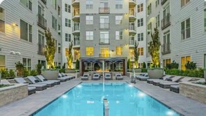 A rectangular swimming pool with a diving board in the center, surrounded by lounge chairs and a covered seating area with umbrellas. - Elite Resort Home • Pool, Jacuzzi, Basketball • Sleeps 16+ King Beds•Shuttle (Everett)