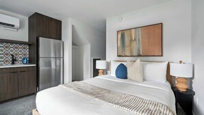 Una habitación de hotel moderna con una cama grande, una zona de cocina y un cuadro en la pared.