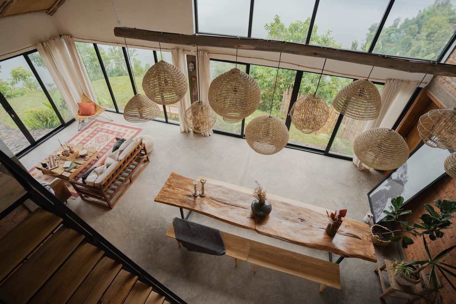 Une pièce spacieuse avec une grande table en bois, des luminaires suspendus en fibres tressées et une vue sur la verdure grâce à de grandes fenêtres.