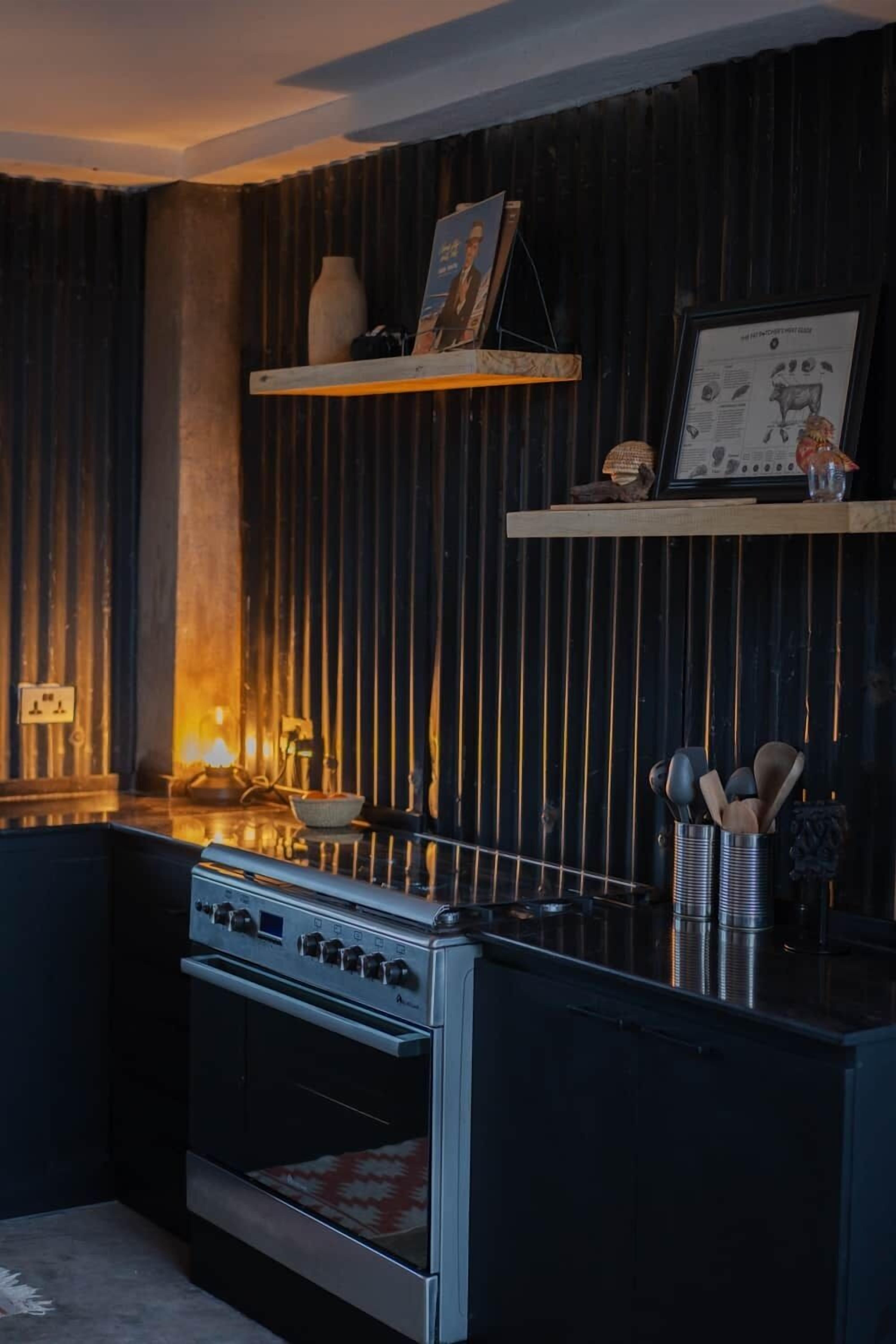 A kitchen with a stainless steel stove, a wooden shelf with decorative items, and a black textured wall.