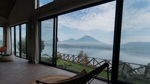 A room with large windows offering a view of a lake and a mountain. - The Writer's Patch - Two bedroom house on lake  Ruhondo (Musanze)