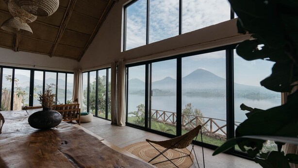 A spacious room with large windows offering a view of a lake and mountains. - The Writer's Patch - Two bedroom house on lake  Ruhondo (Musanze)