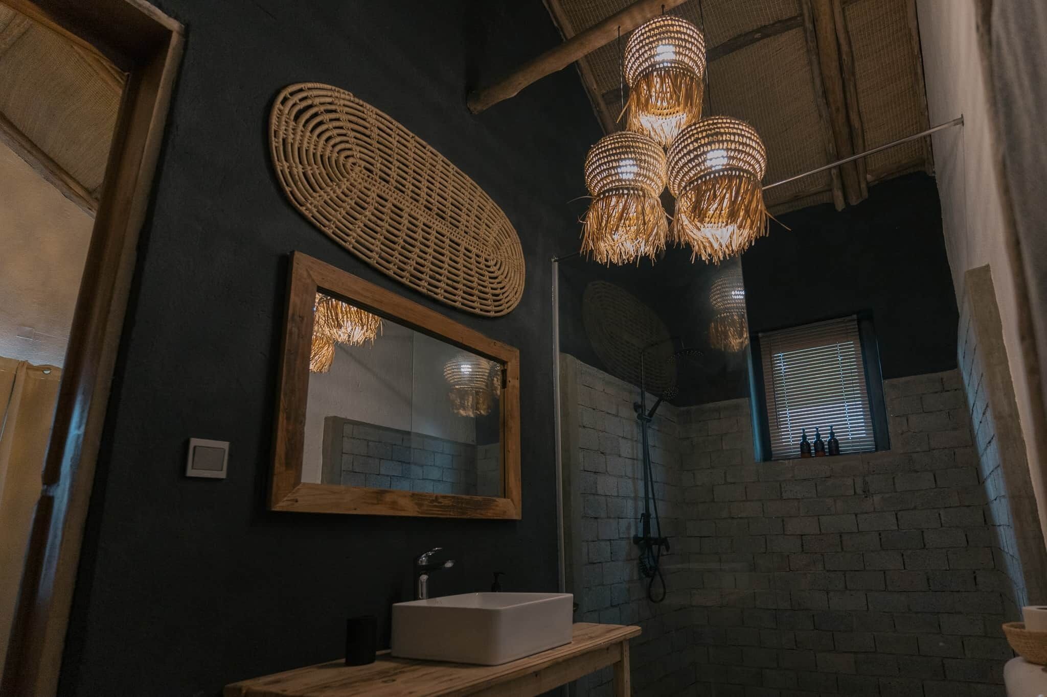 A bathroom with a wooden vanity, a large mirror, and a woven light fixture.