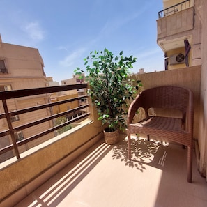 A balcony with a wicker chair, a potted plant, and a view of neighboring buildings.
