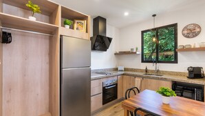 Eine moderne Küche mit einem Edelstahl-Kühlschrank, einem eingebauten Ofen und Holzschränken. Ein Fenster bietet Blick auf Bäume, und an der Wand hängt eine Uhr.