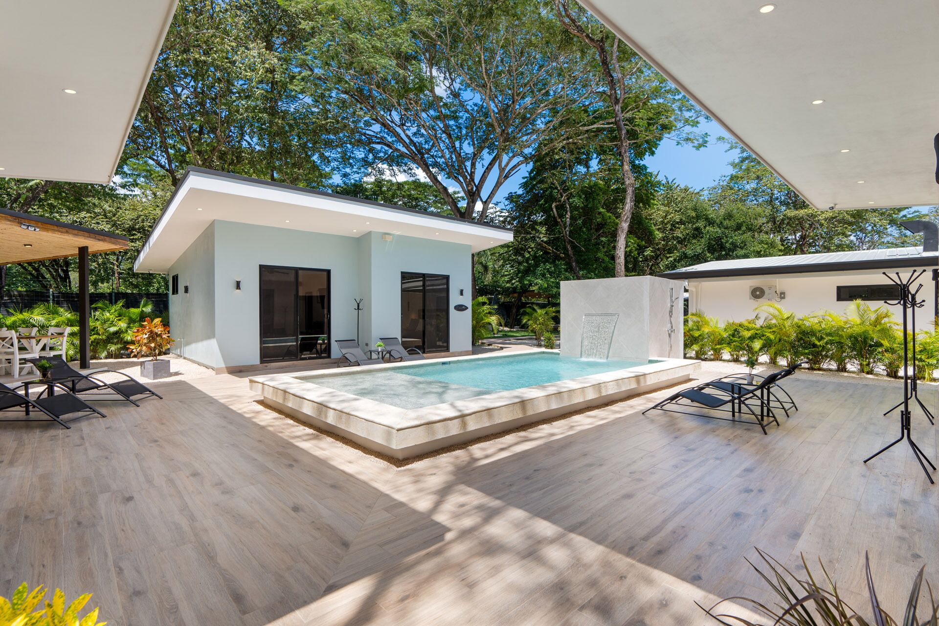 A modern outdoor pool area with a small building, lounge chairs, and a covered seating area.