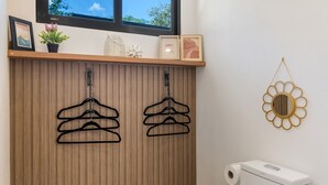 Ein Badezimmer mit Holzvertäfelung, zwei schwarzen Kleiderbügeln, einer Toilette und einem Ziertspiegel.