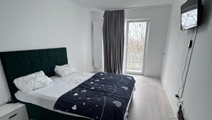 Una camera da letto moderna con un letto, un comodino, una TV a parete e una finestra con tende.