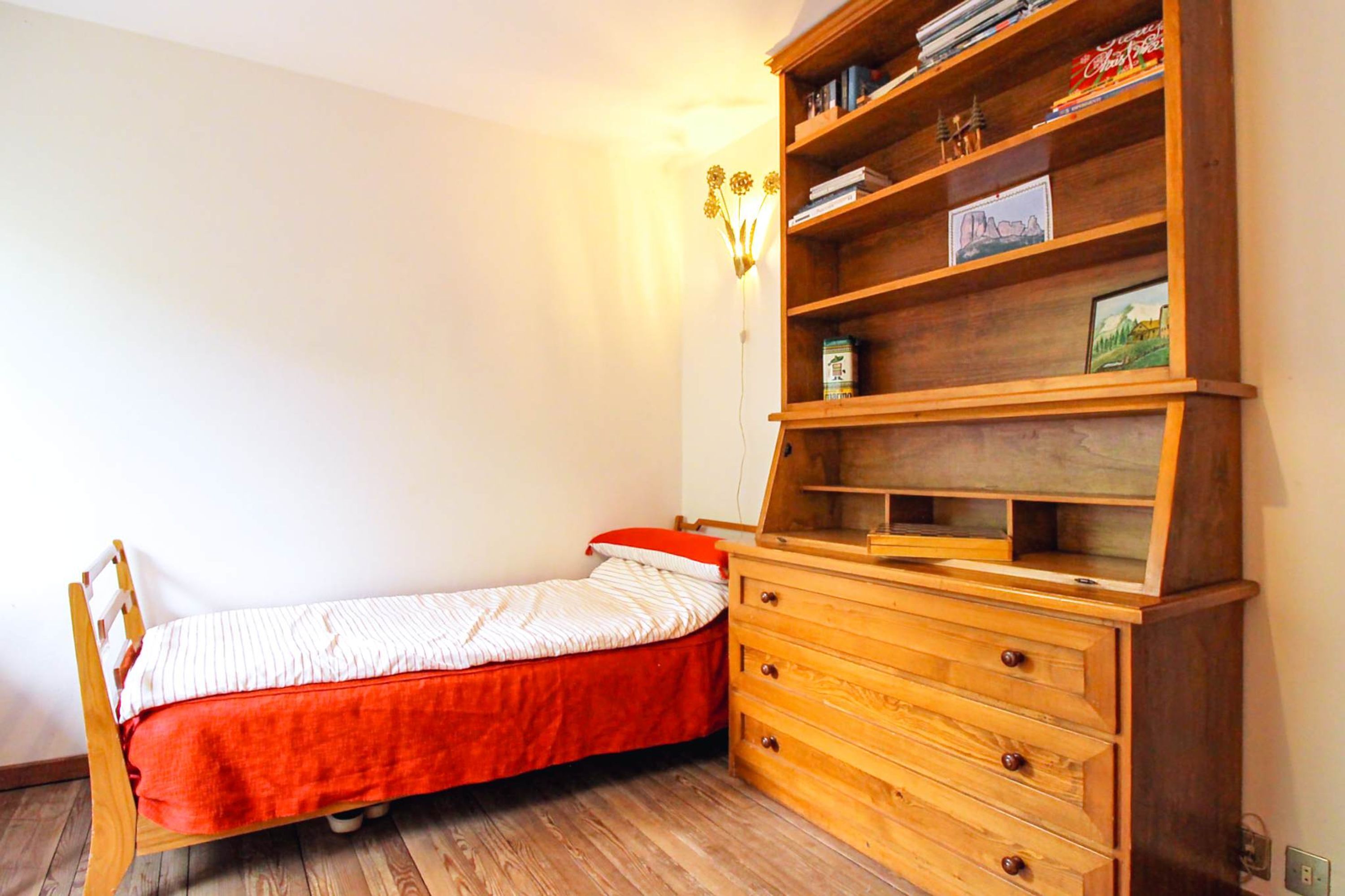 A small bedroom with a single bed, a wooden dresser, and a bookshelf.