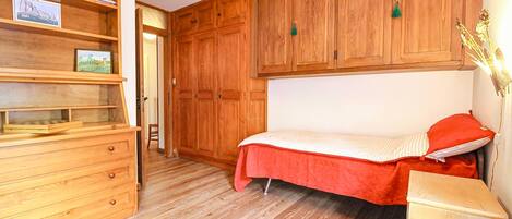A wooden room with a bed, a dresser, and a shelf with books and pictures.