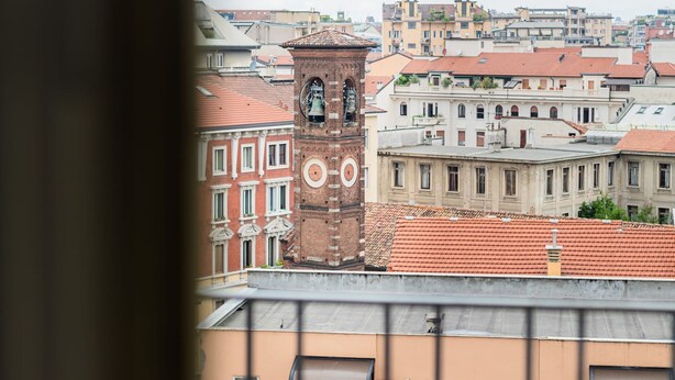 Una vista dello skyline urbano, con una torre dell'orologio imponente e edifici tradizionali dai tetti in tegole rosse.
