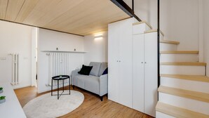 Un soggiorno moderno con pavimento in legno, un divano grigio, un termosifone bianco e una scala con gradini in legno.