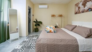 Ein Schlafzimmer mit einem Bett, einer hängenden Pflanze, einer Weltkarte an der Wand und einem gemusterten Teppich.