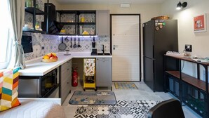 Eine kompakte Küche mit weißer Arbeitsplatte, schwarzen Schränken und einem schwarzen Kühlschrank. Es gibt eine kleine Essecke mit Tisch und Stühlen.