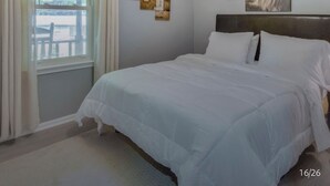 Un dormitorio con cama, ventilador de techo, ventana con cortinas y una obra de arte en la pared.