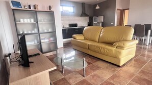 A modern living room with a glass coffee table, a yellow sofa, and a kitchen area in the background. - La Cuadra, where time stands still. (El Time)