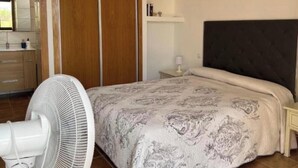 A bedroom with a bed, a nightstand, a bedside lamp, a fan, and a wardrobe. - La Cuadra, where time stands still. (El Time)