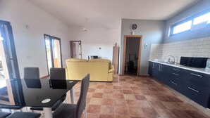 A modern kitchen with dark cabinets and a tiled backsplash, a dining area with a black table and chairs, and a yellow sofa in the living area. - La Cuadra, where time stands still. (El Time)