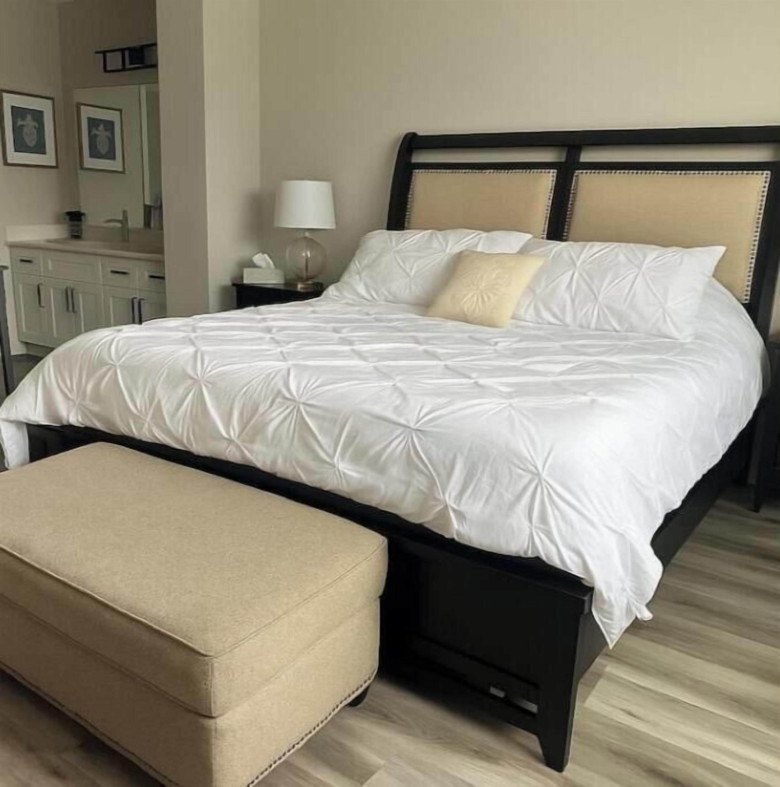 A neatly made bed with a matching bench, a bedside table with a lamp, and a dresser with framed pictures.