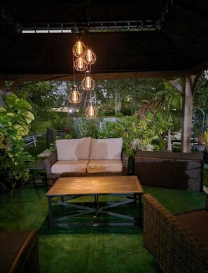 An outdoor seating area with a sofa and a coffee table, surrounded by lush greenery and hanging light fixtures. - Charming centrally located 2-bedroom house with oversized backyard and gazebo. (Miami)