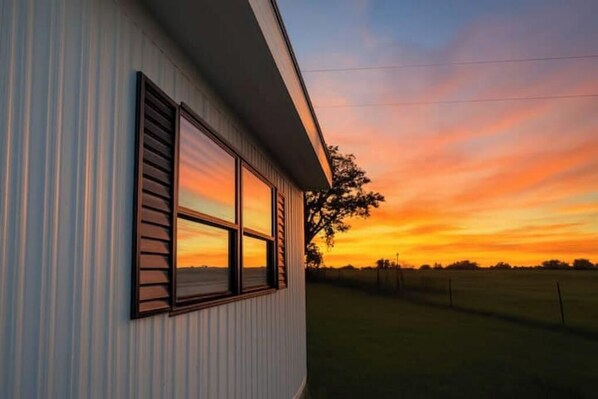 A building with a large window overlooking a field during sunset.