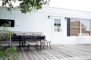 A white building with a wooden deck, a black sofa, and a white chair.