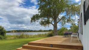 A wooden deck with steps leading to a seating area, overlooking a lake and surrounded by greenery. - -The Villa On The Lake- (Groveland)