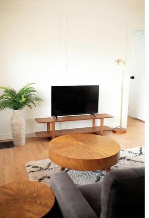 A modern living room with a flat-screen TV on a wooden stand, a round wooden coffee table, a grey sofa, and a potted plant.