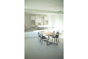 Ein modernes, minimalistisches Zimmer mit einem großen Bett, integrierten Regalen und einem Essbereich mit Tisch und Stühlen.
