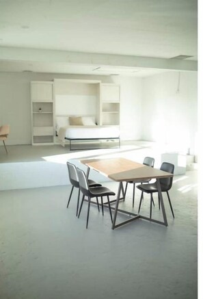 A modern, minimalist room with a large bed, built-in shelving, and a dining area with a table and chairs.