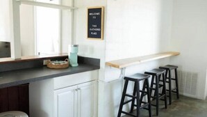 A kitchen with a bar area, white cabinets, a welcome sign, and bar stools.