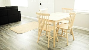 A dining area with a wooden table and four chairs, a black sofa, and a wooden floor.