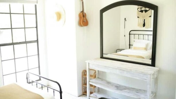Een slaapkamer met een bed, nachtkastje, spiegel en een gitaar aan de muur.