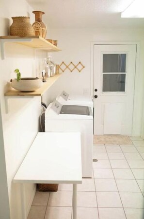 A laundry room with a washing machine, a dryer, and shelves with baskets and bottles.