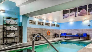 A swimming pool with a metal ladder, blue cushioned seating, and a shelf with towels. - Exciting Rockies 1BR Escape, Hot Tub, Pool & BBQ! (Canmore)