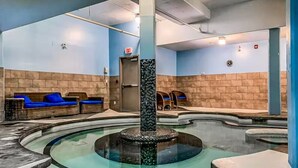 A pool area with a central fountain, blue seating, and a brick wall. - Exciting Rockies 1BR Escape, Hot Tub, Pool & BBQ! (Canmore)